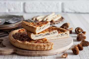 Quiche - tart pie with spring morel mushrooms, onion and cheese on wooden cutting board