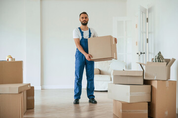 Full height photo, standing and holding big box. Moving service employee in a room