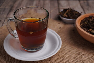 cup of black tea with saucer as base and dried tea leaves on side as ornament