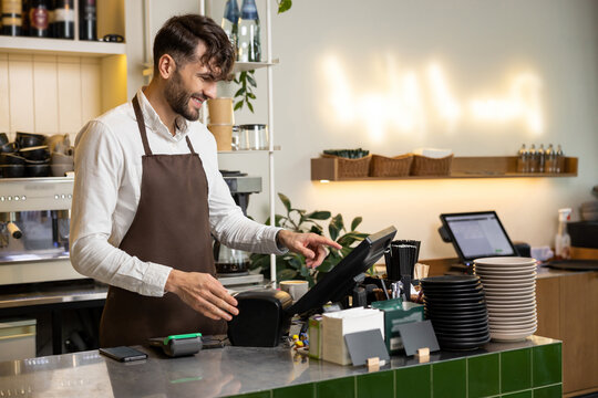 Man waiter working in coffee shop using terminal while standing at counter