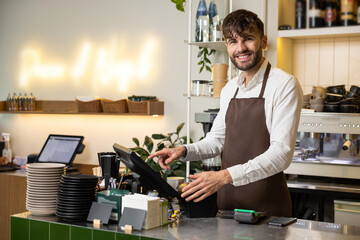 Waiter man working in coffee shop using terminal for checking orders standing at counter