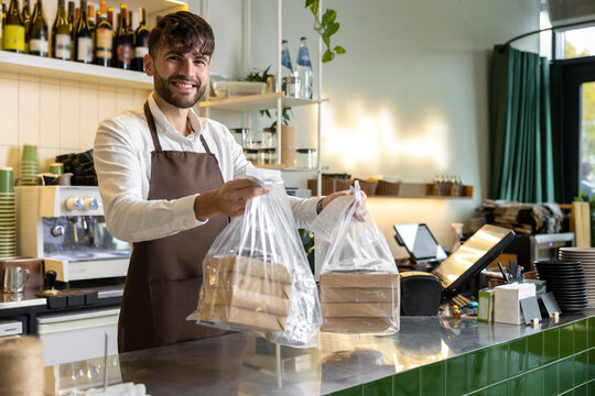 Young bearded man bartender holding fresh pizza in boxes in pizzeria