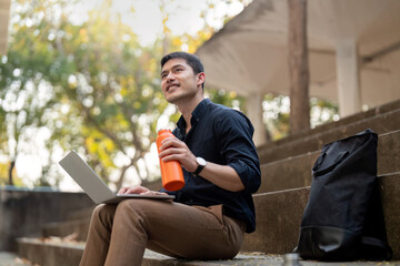 Asian businessman with reusable eco friendly ecological cup using laptop and sitting outside the...