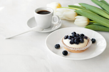 Delicious and sweet morning breakfast, panna cotta cookie dessert with blueberries, coffee cup and white flowers on table