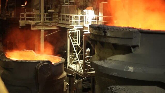 Molten metal being poured in foundry, intense orange glow, industrial setting, heat and smelting process, night shot
