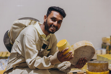 Portrait of happy young Indian beekeeper holding wax and honey and working in beekeeping factory