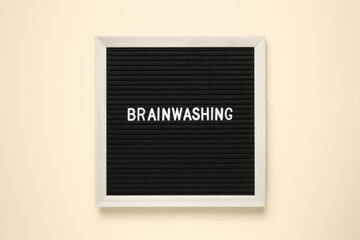 The word brainwashing on black letter board over isolated beige background.