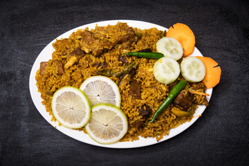 Fototapeta na wymiar Beef Yakhni biryani rice pulao with cucumber, lime slice and carrot served in dish isolated on dark background top view indian spices, bangladeshi and pakistani food