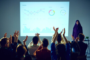 Corporate training session surrounded by data visualizations where woman ending speech and audience clapping raising hands. Concept of business, startup, leadership and personal development courses.