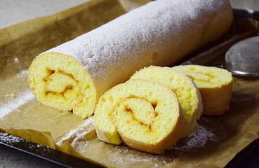 Sponge cake filled with jam and icing sugar sprinkled on a baking sheet	