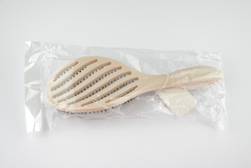 New beige oval hairbrush with bristles and a white tag in a transparent plastic package on a white...