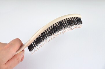 New beige oval hairbrush with bristles in a hand on a white background