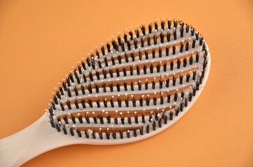 New beige oval hairbrush with bristles on an orange background, closeup