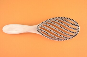 New beige oval hairbrush with bristles on an orange background, top view