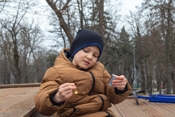 A mischievous child  outdoors holds a burning match and a matchbox in his hands. Danger of fire for children. Close-up image