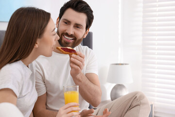 Fototapeta premium Tasty breakfast. Happy husband feeding his wife in bedroom. Space for text