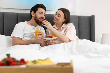Obraz na płótnie Canvas Tasty breakfast. Happy wife feeding her husband in bed at home