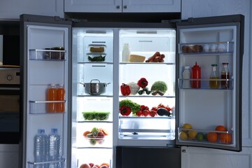 Open refrigerator full of different products in kitchen