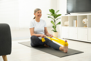 Senior woman doing exercise with fitness elastic band on mat at home