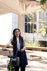 Eco friendly, Happy lifestyle asian beautiful young businesswoman riding bicycle go to office work at city street with bicycle in morning