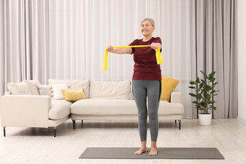 Senior woman doing exercise with fitness elastic band on mat at home