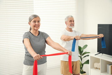 Obraz premium Senior couple doing exercise with fitness elastic bands at home, selective focus
