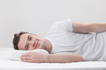 Man lying on orthopedic pillow against light grey background