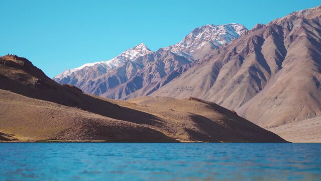 4K Landscape shot of Chandra Taal Lake in front of the snowy Himalayan mountain peaks near Kunzum Pass in Spiti Valley, Himachal Pradesh, India. Water of the Chandra Taal lake moves due to wind. 