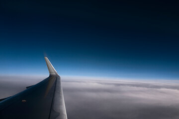 Airplane wing at a great height against clear and cloudy blue sky.  Useful horizontal banner