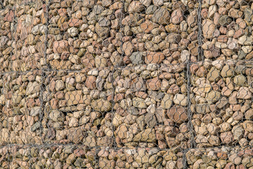 engineering structure made of stones behind metal wire netting to strengthen the river bank near the road bridge