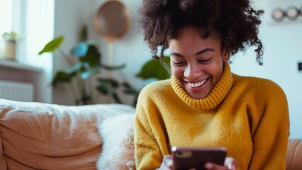 An African American woman wearing a yellow sweater texting on a smartphone while working in the living room.