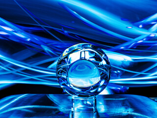 Glass ball on a metal surface, dark background with blue dynamic ight painting. Fortune telling or...
