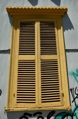 Rustic wooden yellow shuttered window on a pale blue corrugated metal house. 