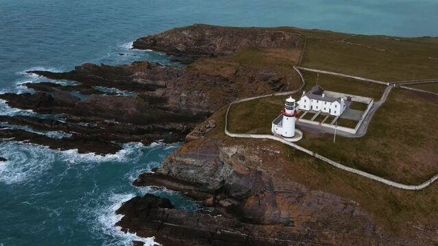 drone flying over a white lighthouse and rocks, ocean view, Ireland