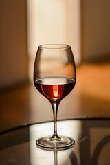 Single elegant glass of rose wine on the glass table indoor with shadows. Minimalist creative composition. Wine tasting.