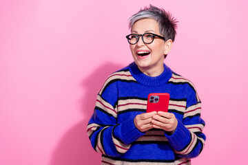 Fototapeta premium Photo of attractive pensioner woman hold device look empty space dressed stylish blue striped clothes isolated on pink color background