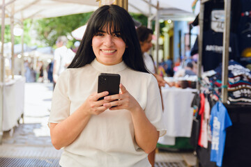 young happy woman tourist outside at crafts fair in Argentina using phone