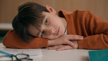 Caucasian bored schoolboy sleepy at school elementary education study learning tired exhausted sad upset fatigued child boy kid pupil schoolchild lying at table desk lesson class relax health problem