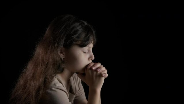Child praying. Little girl prays on a black background.