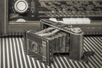Vintage camera. Retractable accordion lens. Against the background of an old tube radio. Black and...