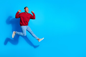 Fototapeta na wymiar Full length photo of carefree delighted person jump raise fists success empty space isolated on blue color background