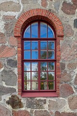 Fototapeta na wymiar Window with red frame with red brick arch on a old stone building.