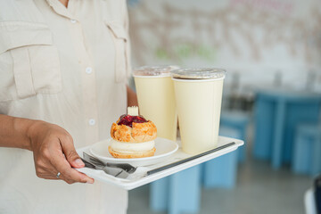 Close up and selective focus hand of employee girl holding tray of scone and coffee at cafe.
