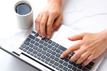 コーヒーを飲みながらノートパソコンでデスクワークをしている会社員のイメージ
