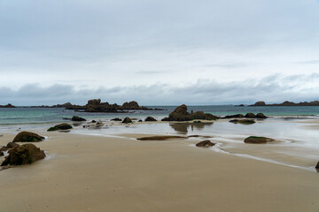 Fototapeta na wymiar Plage de sable et rochers sous un ciel nuageux : la côte des Légendes en Bretagne dévoile toute sa majesté