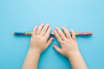 Baby boy hands rolling colorful stick from modeling clay on light blue table background. Pastel...