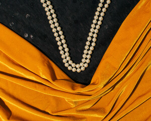 Amber yellow velvet fabric, draped, pearl necklace composition on black background, feminine...