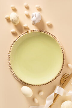 Easter table setting with green plate, decorative eggs and bunny on beige background. View from above. Vertical format.