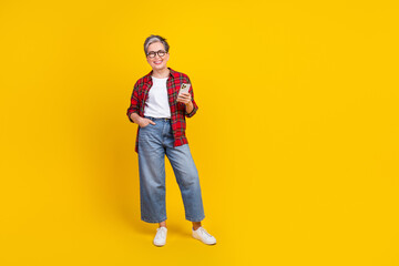 Fototapeta premium Full size photo of cheerful grandmother hold smart phone empty space ad isolated on yellow color background