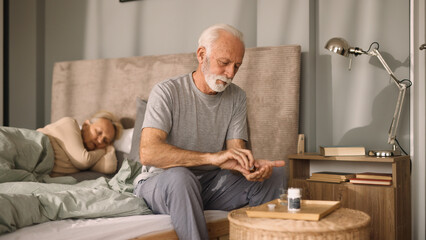 Elderly man taking medication with water in bedroom